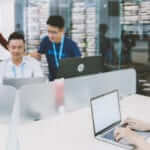 The cloud for continuous delivery image shows a man working on a laptop in the foreground. In the background you see three people working around one computer. A man sits in the middle. On his left is a woman, standing and on his right is a man, standing. All three wear KMS lanyards.