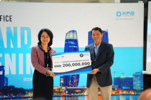A man and woman stand next to each other in front of a banner with the KMS logo and Da Nang skyline. Both are holding a large check for 200,000,000 VND.