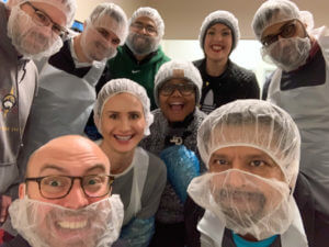 In a group selfie, members of the KMS team are seen smiling and wearing mesh hairnets. Those with beards also have nets that cover the lower half of their face.