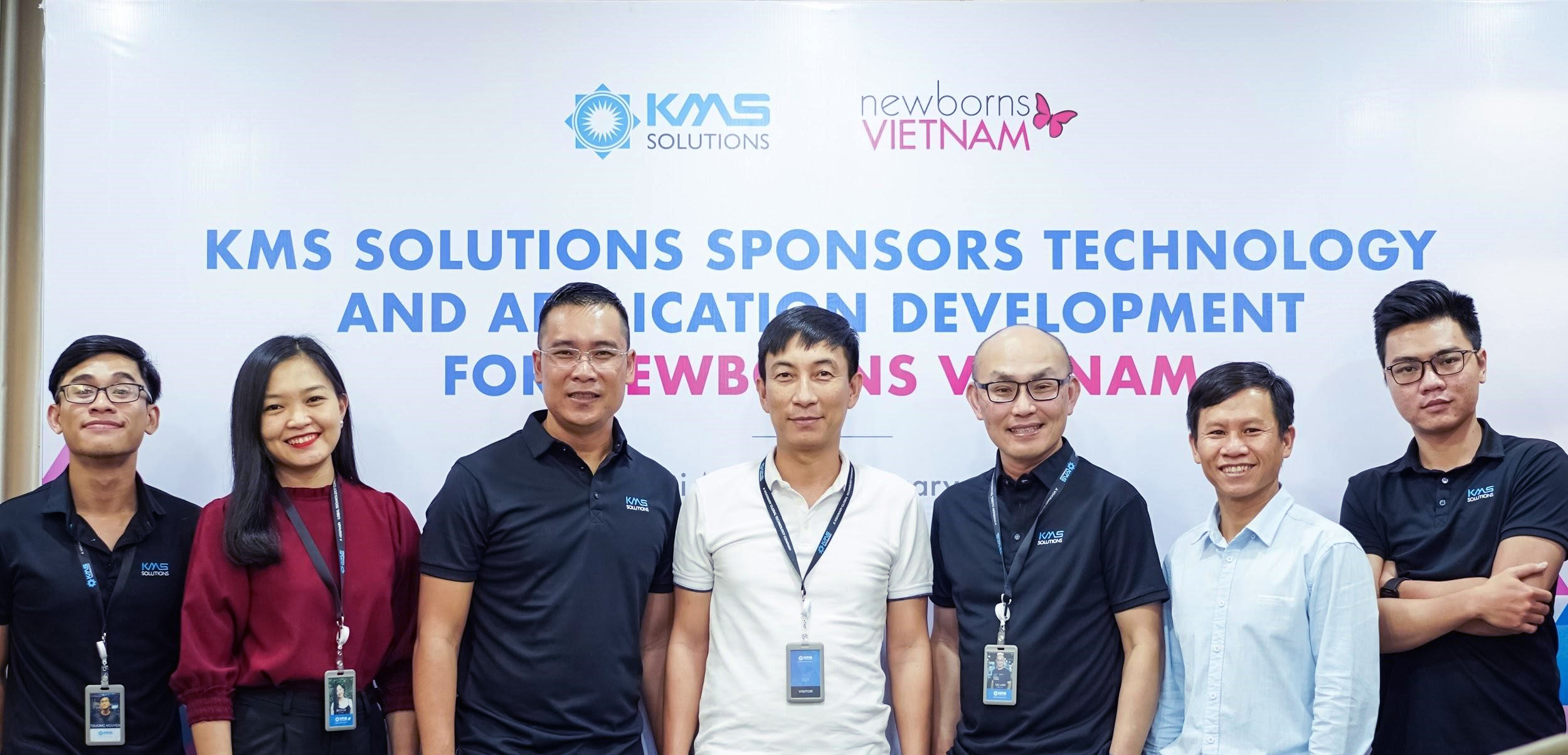 The KMS team stands in front of a banner reading "KMS Solutions sponsors technology and application development for newborns Vietnam."
