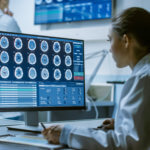 The benefits of AI in healthcare hero shows a female doctor looking at a computer screen. On the screen are a series of brain scans.